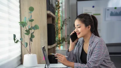 A woman on a phone call while working on a tablet in a modern office setting.