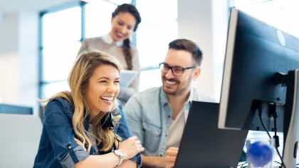 Group of cheerful colleagues collaborating in a modern office setting with computers.