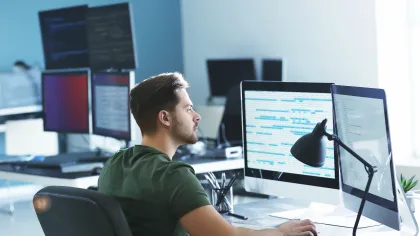 A focused man working at a desk with multiple computer monitors in a modern office setting.