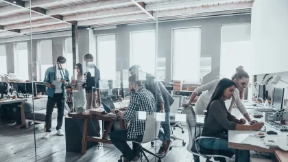A modern office with coworkers collaborating at desks, showcasing teamwork in a bright space.