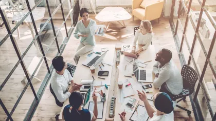 Team brainstorming in a modern meeting room with laptops and documents on a large table.