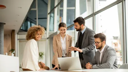 Four professionals collaborating around a laptop in a modern office setting.