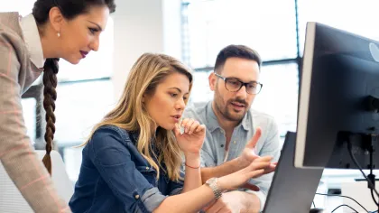 Three professionals collaborating on a project at a modern office, focused on a computer screen.