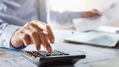 A business professional using a calculator while reviewing financial documents.