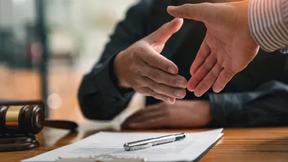 Two hands shaking over a legal document with a gavel in the background, symbolizing agreement and partnership.