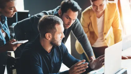 A group of professionals collaborating around a laptop in a modern office setting.