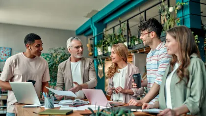 A diverse group of colleagues collaborating in a bright, plant-filled workspace.