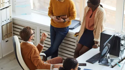 Colleagues collaborating in a bright office with computers and documents on a desk.
