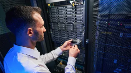 IT technician installing hardware in a data center server rack with blue lighting.