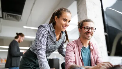 Two colleagues collaborating in a modern office, smiling and engaged with a computer.