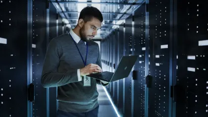 IT professional working on laptop in a modern data center with illuminated server racks.