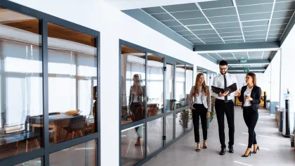 Professionals collaborating in a modern office corridor with large windows and contemporary design.