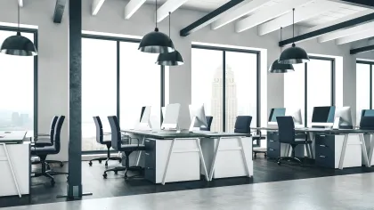 Modern office interior with desks, chairs, and large windows showcasing a city view.