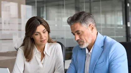 Two professionals discussing documents in a modern office setting with a laptop on the table.
