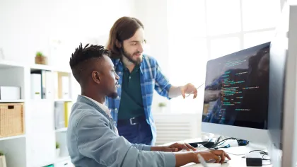 Two men collaborating on coding tasks at a computer in a modern office space.