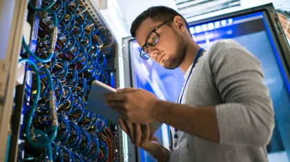 Technician inspecting server connections in a data center with cables and devices in the background.