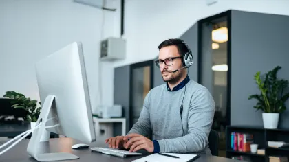 A focused man wearing headphones works on a computer in a modern office setting.