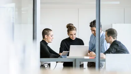 Four professionals collaborating over a laptop in a modern office setting.