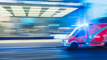 Red ambulance with flashing lights speeding through city streets at night with motion blur effect