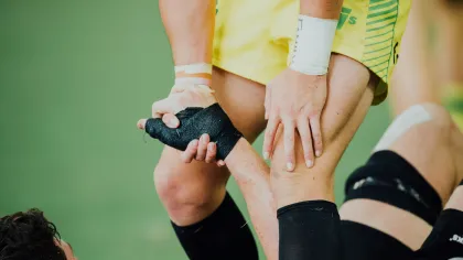 Two rugby players in action gripping each other's wrists during a game, wearing sports tape and uniforms.