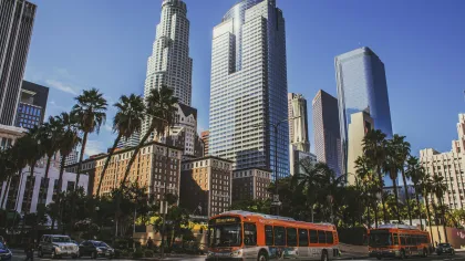 Downtown Los Angeles skyline with palm trees, high-rise buildings, and city buses on a sunny day.