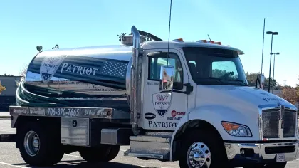 White Patriot branded tanker truck parked in a parking lot on a sunny day with clear blue sky.