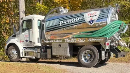 Patriot plumbing and septic service truck parked on driveway near autumn trees with green hoses on tanker.