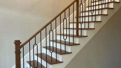 Wooden staircase with black metal balusters and light beige walls in a modern home interior.