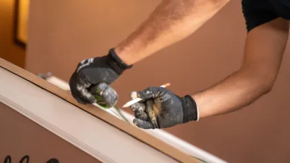Close-up of gloved hands measuring and marking wood with a pencil and tape measure for carpentry work.