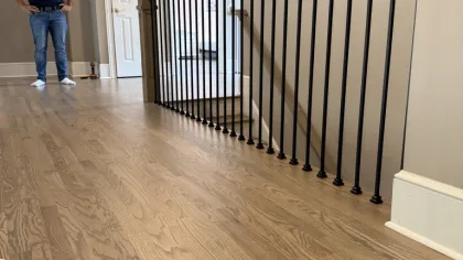 Polished wooden floor and black metal stair railing in a modern light beige hallway with a man standing.