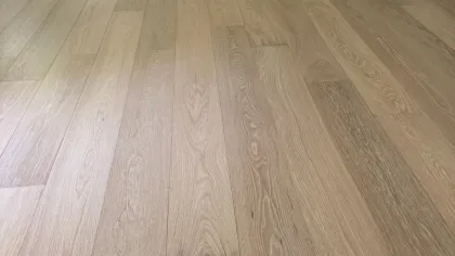 Newly installed light oak hardwood flooring in an empty room with gray walls and an open white door.