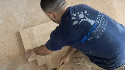 Man installing wooden flooring panels kneeling with a rubber mallet on a cork underlayment floor.
