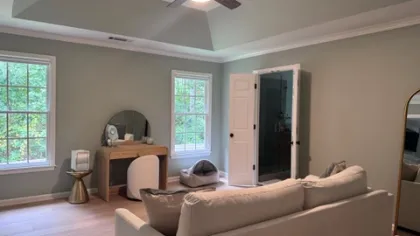 Modern living room with a beige sofa, wooden vanity, ceiling fan, and large windows with natural light