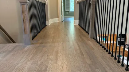 Indoor hallway with light wood flooring, beige walls, and black metal railing on both sides leading to a room.