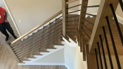 Top view of modern wooden staircase with black metal railing inside a home with light wood flooring.