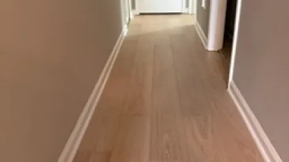 Narrow hallway with light wood flooring, beige walls, and a closed white door at the end.