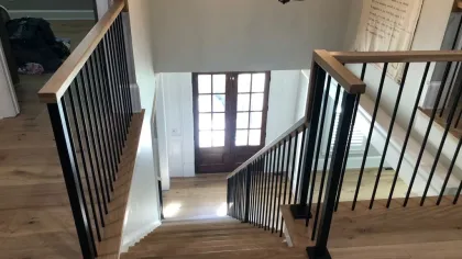 Modern wooden staircase with black metal railings leading to a bright entrance door with glass panels.