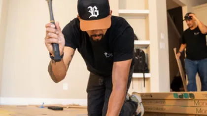 Construction worker installing wooden flooring using a rubber mallet in a residential interior setting.