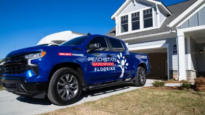 Blue Peachstate Hardwood Flooring truck parked in driveway of modern white house on a sunny day