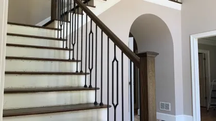 Wooden staircase with dark railing and white risers in a spacious home entryway with arched doorway and chandelier