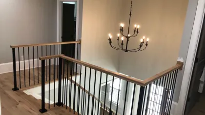 Modern staircase with wooden handrails and black metal balusters under a black metal chandelier with lit bulbs