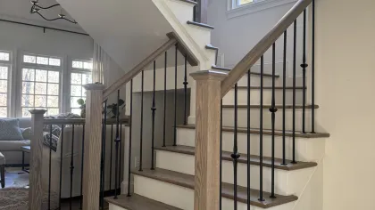 Modern wooden staircase with black metal balusters in a bright living room with large windows.