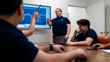 Man presenting refining process roadmap to colleagues in a meeting room with a digital screen.