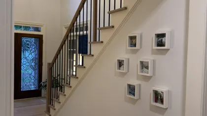Modern staircase with wooden steps, black railings, small picture frames on white wall, chandelier, and glass front door.