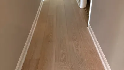 Narrow hallway with light wood flooring and neutral beige walls leading to a white door with black knob.