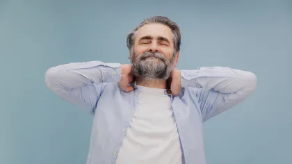 Smiling mature man with beard stretching and relaxing with eyes closed against blue background