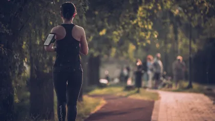 Woman jogging on a tree-lined path wearing black athletic wear with blurred park visitors in the background.