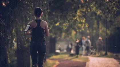 Woman jogging on a tree-lined path wearing black athletic wear with blurred park visitors in the background.