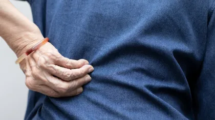 Elderly person gripping their side in pain wearing a blue shirt and a wristband close-up.