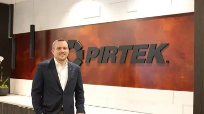 Man in business attire standing next to a wall with large PIRTEK logo and modern office decor.